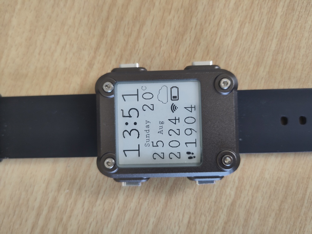 A Watchy with gun metal case displaying the time, date,
weather and a steps count in a custom monospace font.